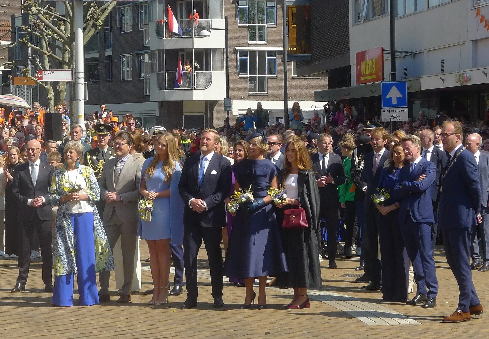 De koninklijke familie staat op straat in Doetinchem, met publiek op de achtergrond