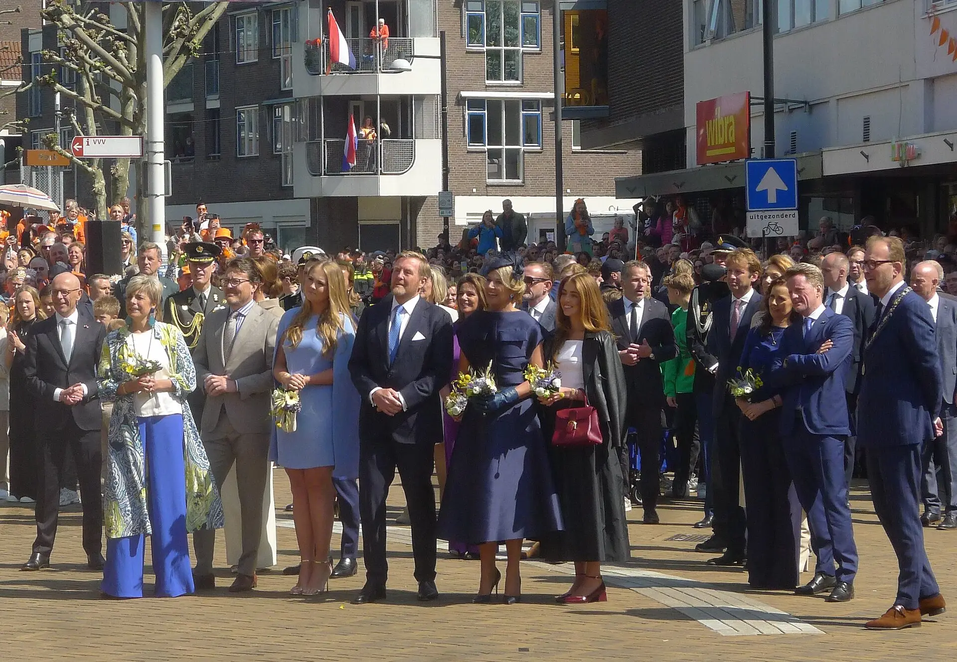 De koninklijke familie staat op straat in Doetinchem, met publiek op de achtergrond