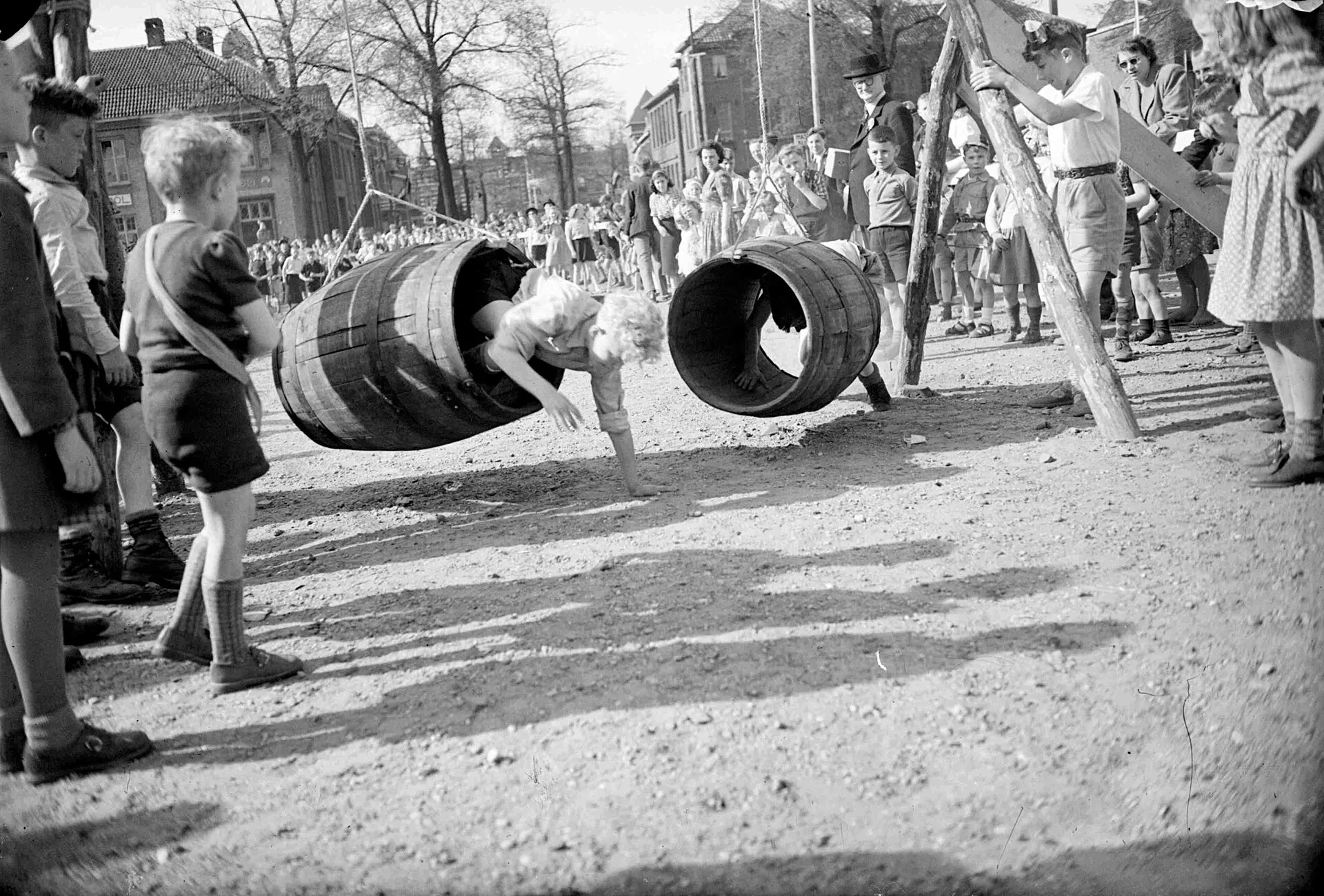 Kinderen kruipen door tonnen bij kinderspelen op Koninginnedag 1950